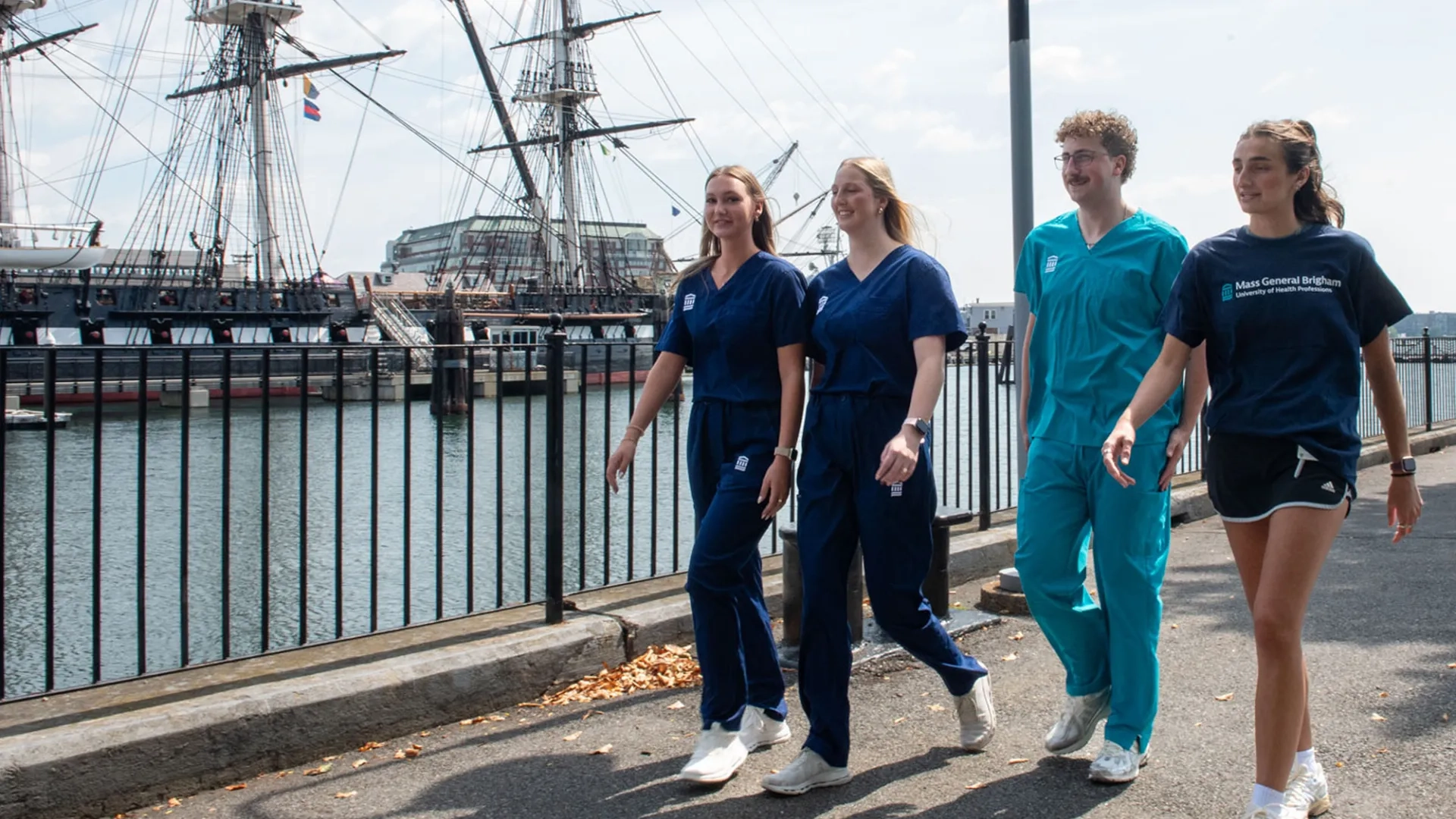 students in scrubs and tshirts walk in front of the constitution ship