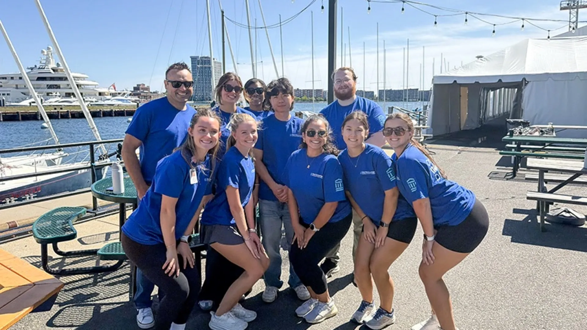 Volunteers in blue shirts posing in front of the Boston Harbor