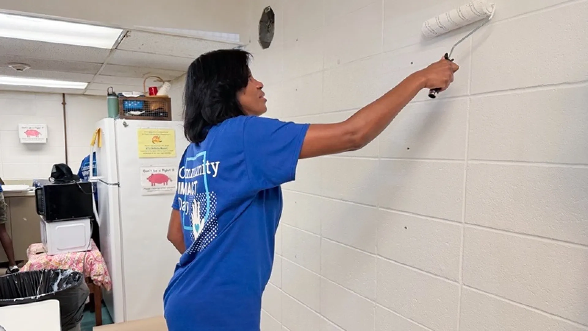 A woman in a blue shirt that reads "Community Impact Day" paints a wall at Harvard Kent Elementary School for Community Impact Day