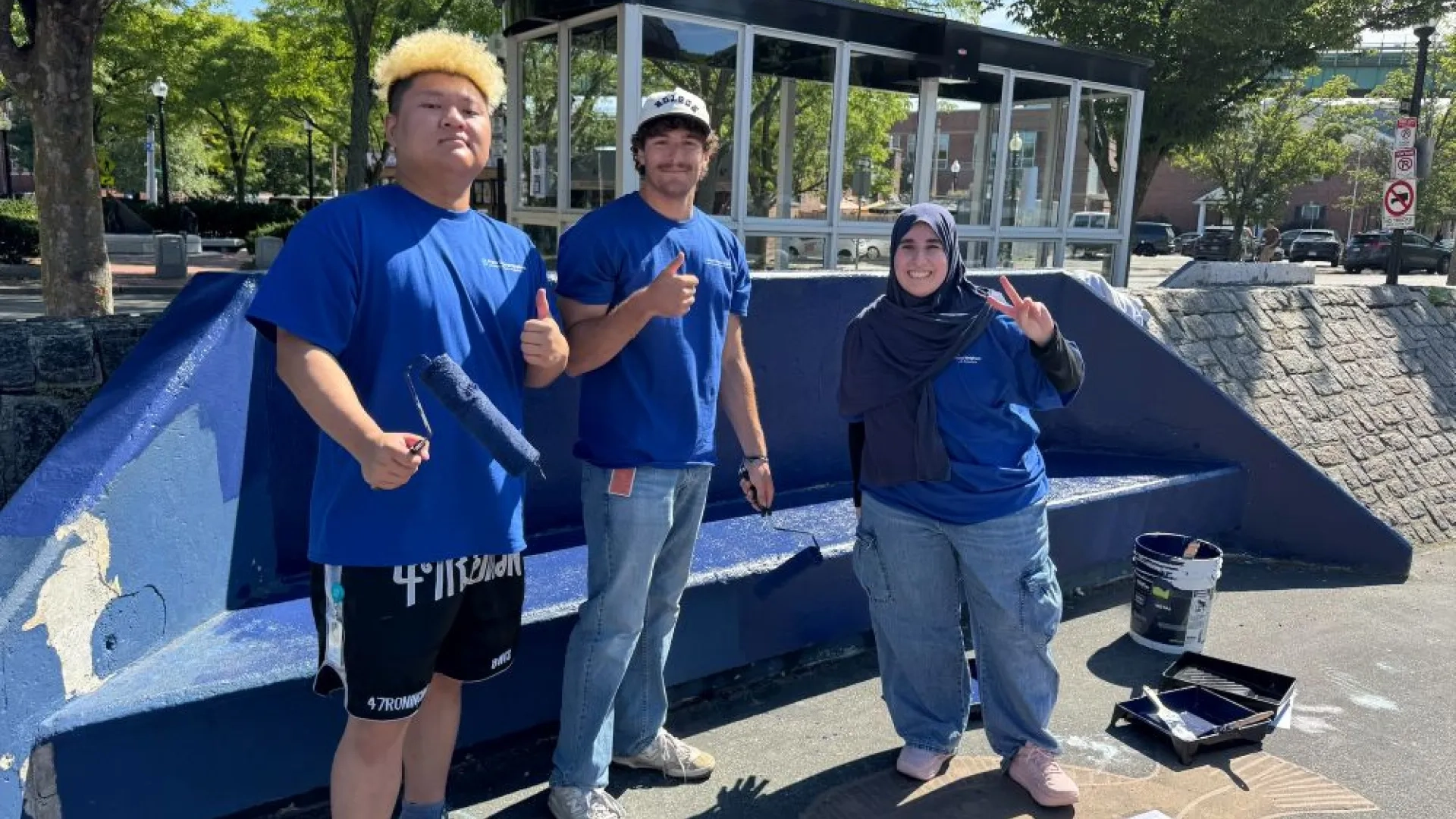 3 individuals standing in front of a freshly painted bench 