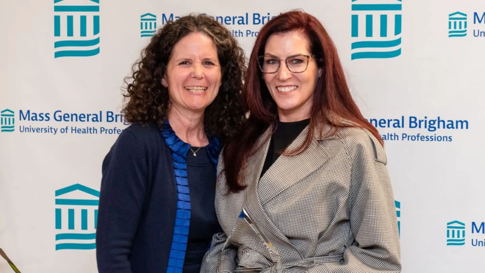 two women posing in front of a branded background