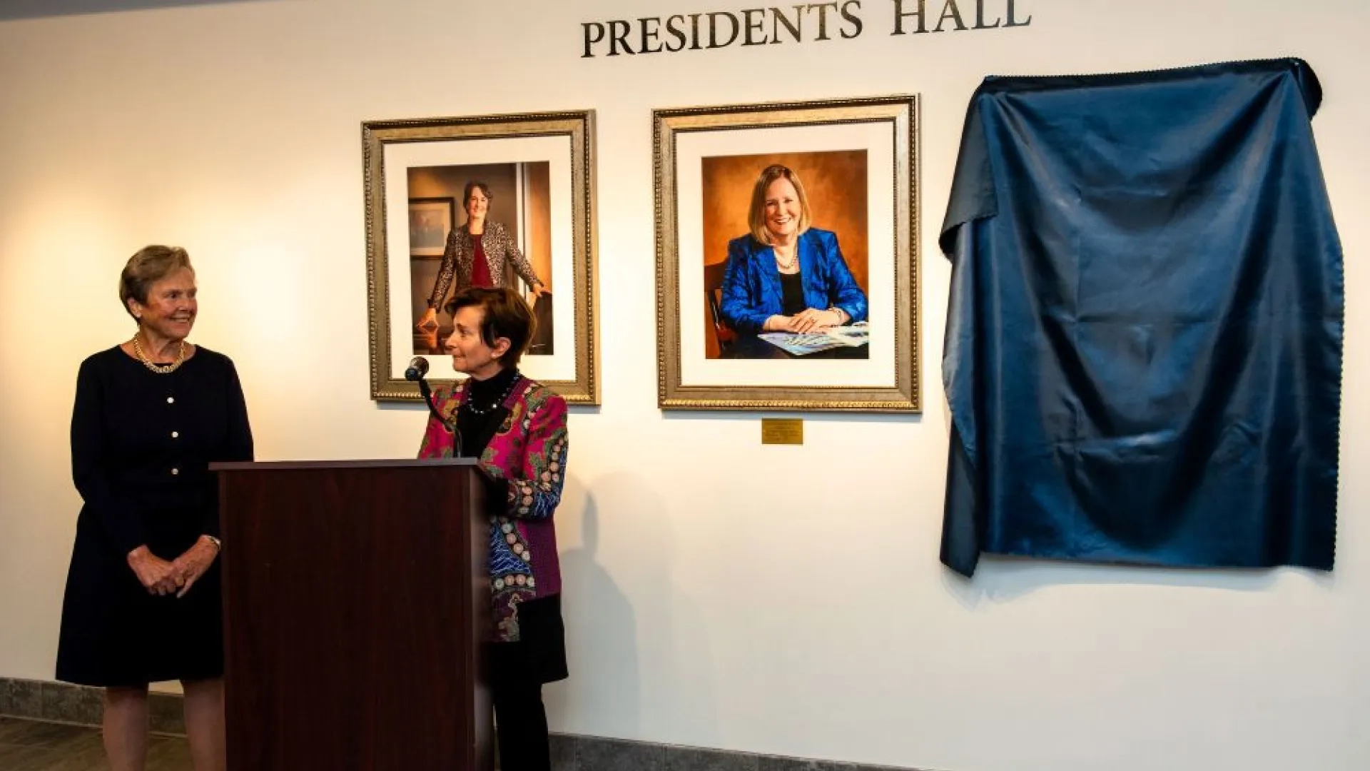 two women standing at a podium in front of portraits