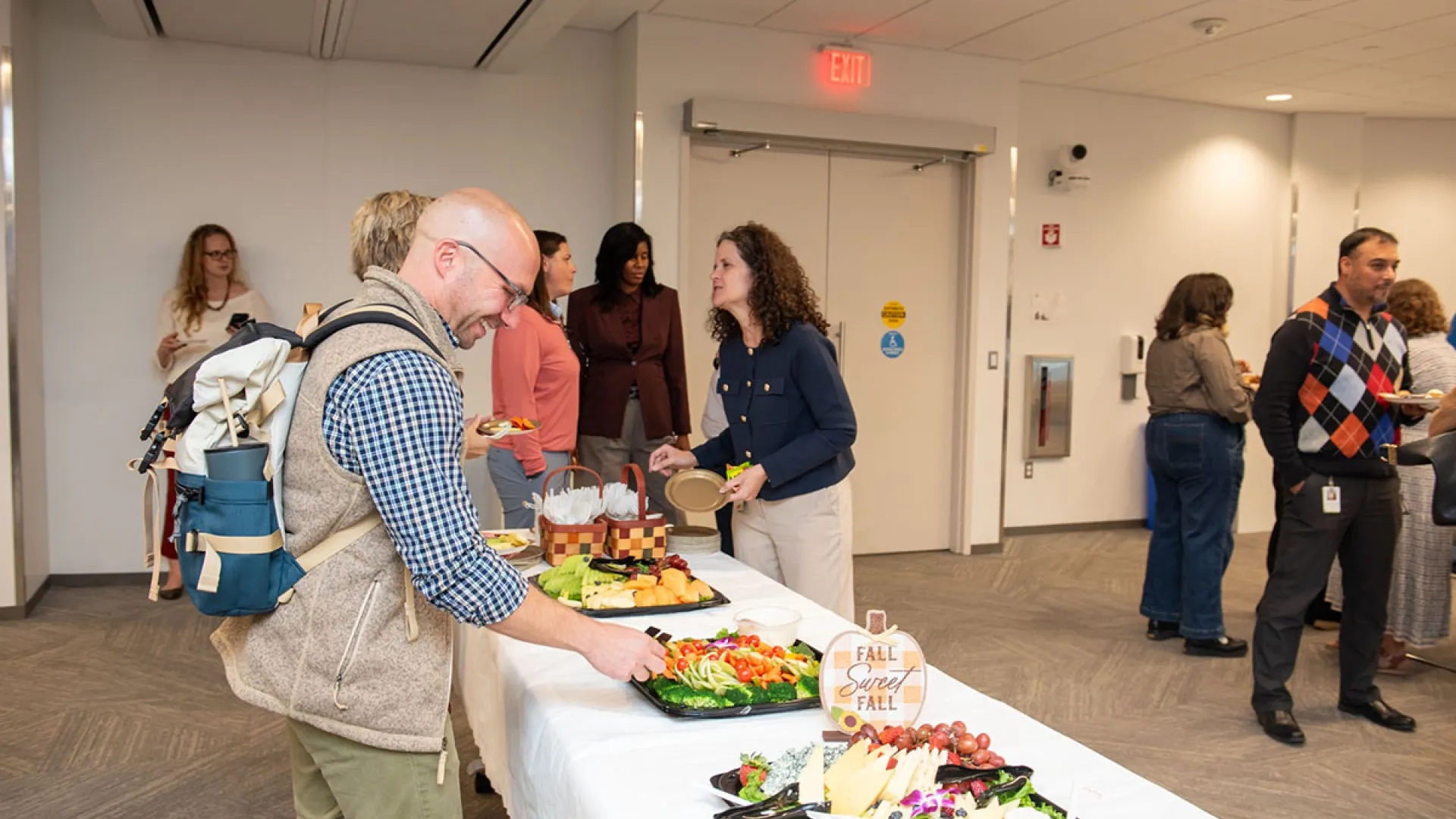A man stands next to a table with food with people in the background