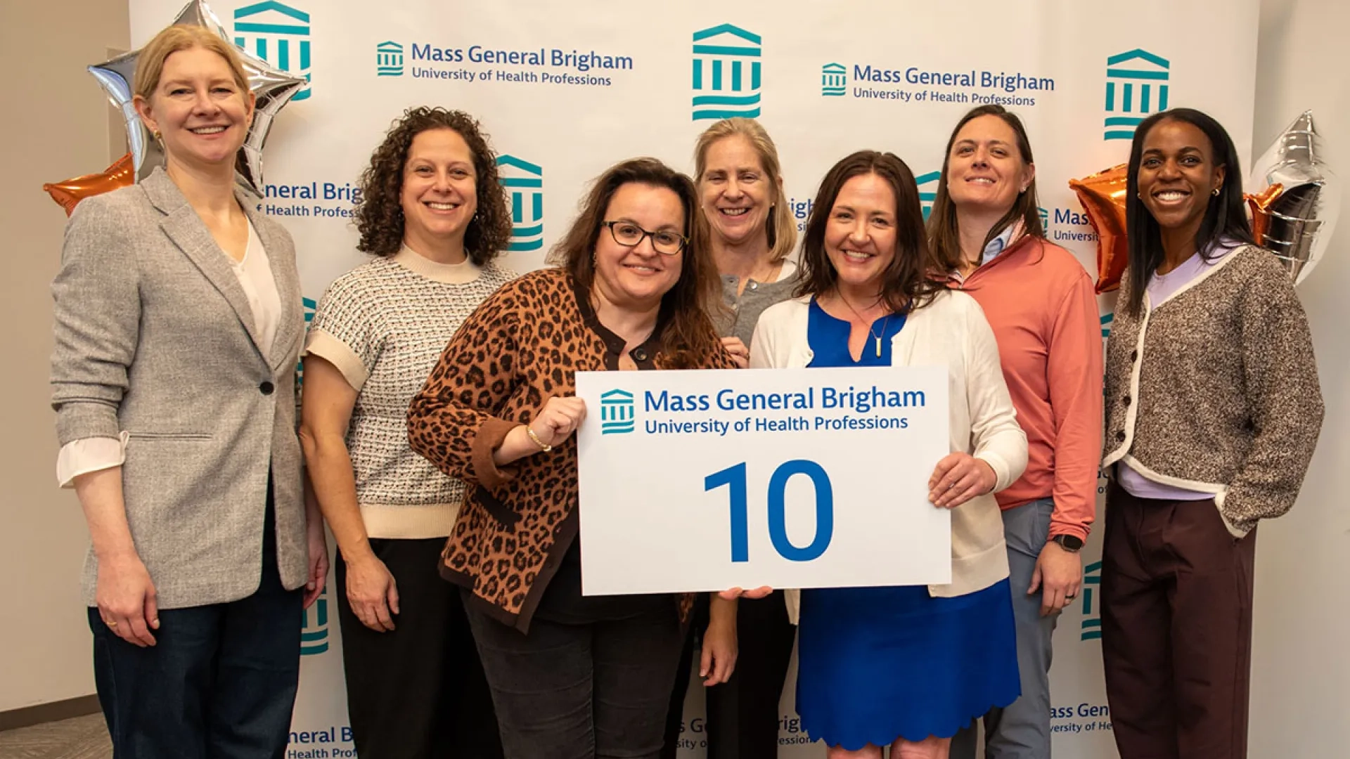 A group stands in front of a Mass General Brigham background holding a sign with the number 10