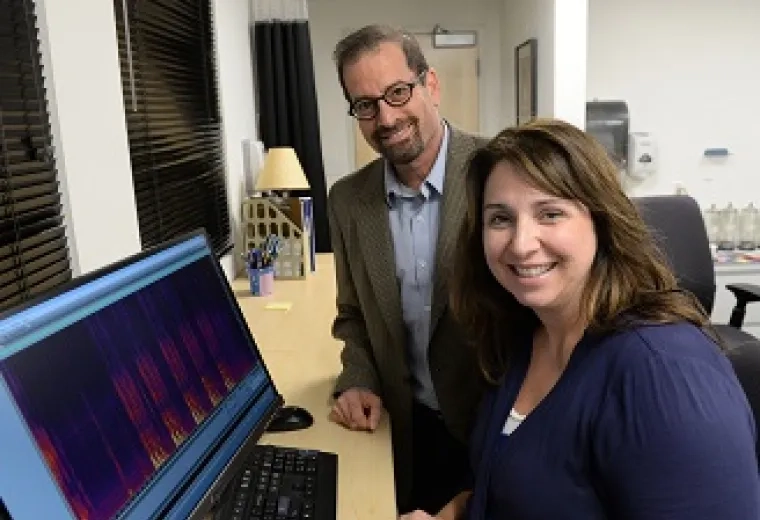  Dr. Jordan Green and Dr. Tiffany Hogan standing in front of a computer monitor, smiling at the camera.