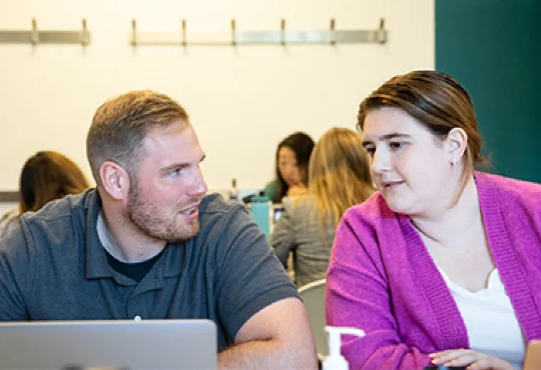 a woman leans over to look at a laptop while a man talks to her