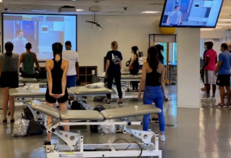 DPT students, adhering to social distancing standards, watch Associate Professor Doug Gross as he works with the other half of the class in an adjacent room.