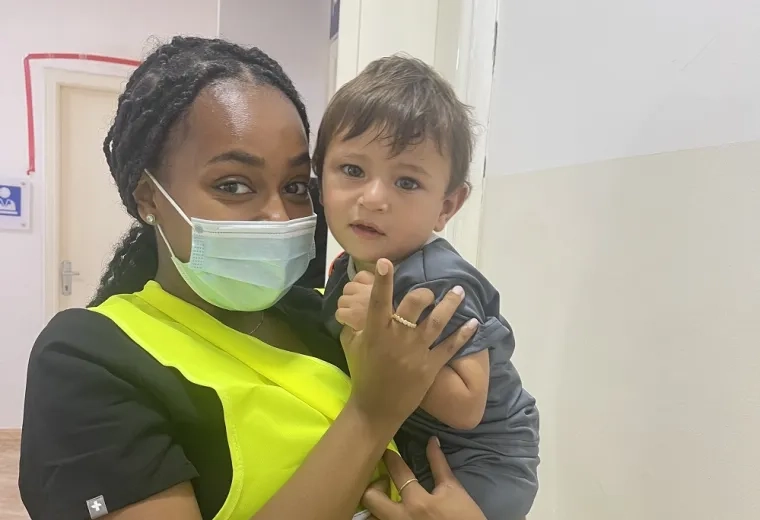 student in yellow vest holds small boy