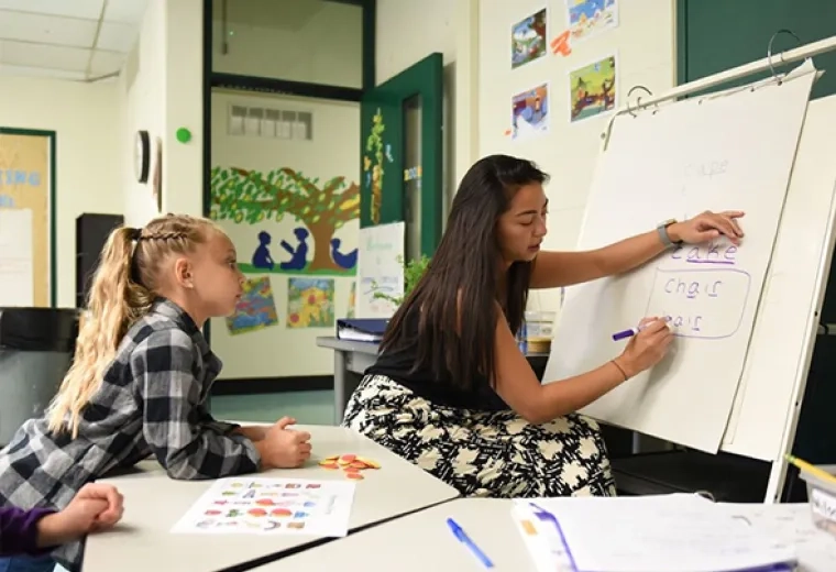 young woman writes letters on a paper easel in an elementary classroom