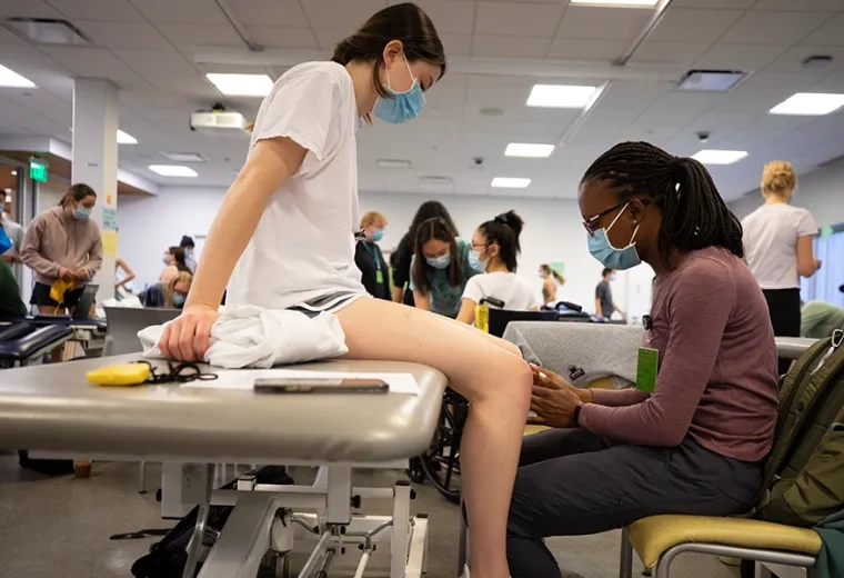 students in mask work together one on an exam table the other touching her knee