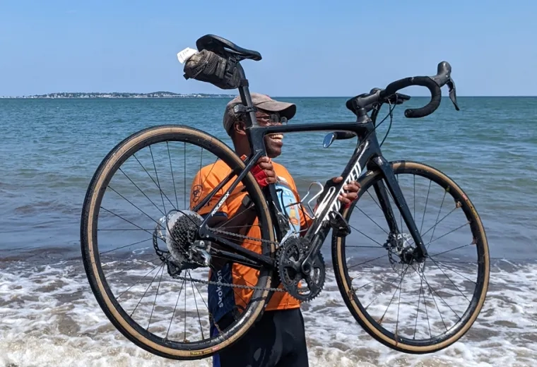 Obel-Omia holds his bike during the celebratory "wheel dip" in Revere, Massachusetts, marking the completion of the cross-country bike journey.