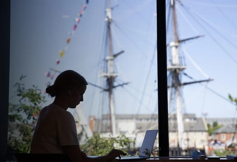 woman sits at laptop with ship mast in the background