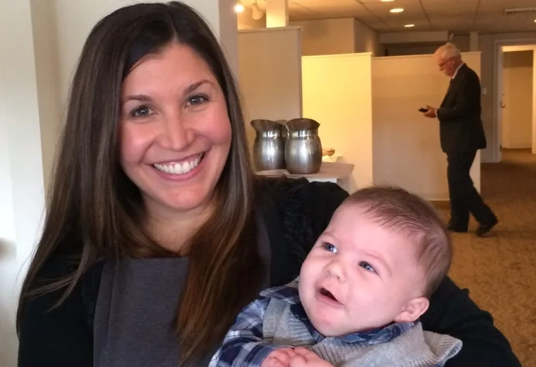 rebecca holds a baby in a sweater vest with a cute puzzled look on his face