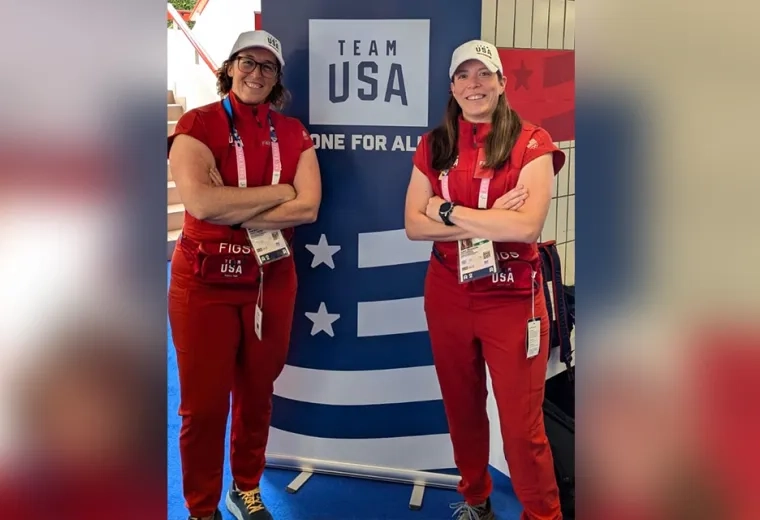 two women in red outfits pose in front of a team USA sign
