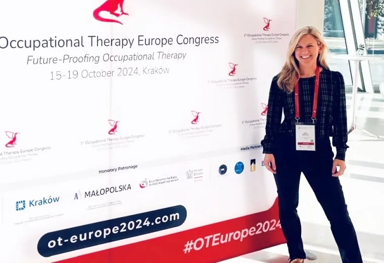 A woman stands in front of a sign for the 1st Occupational Therapy Europe Congress