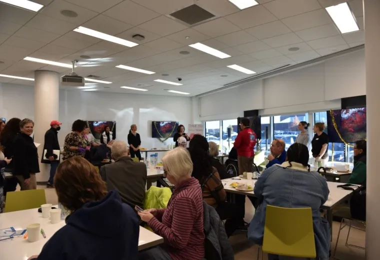 People sit at tables while a woman holding a microphone talks