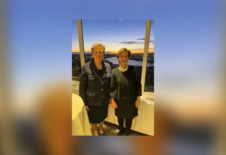 two women stand in front of a nighttime view out a window