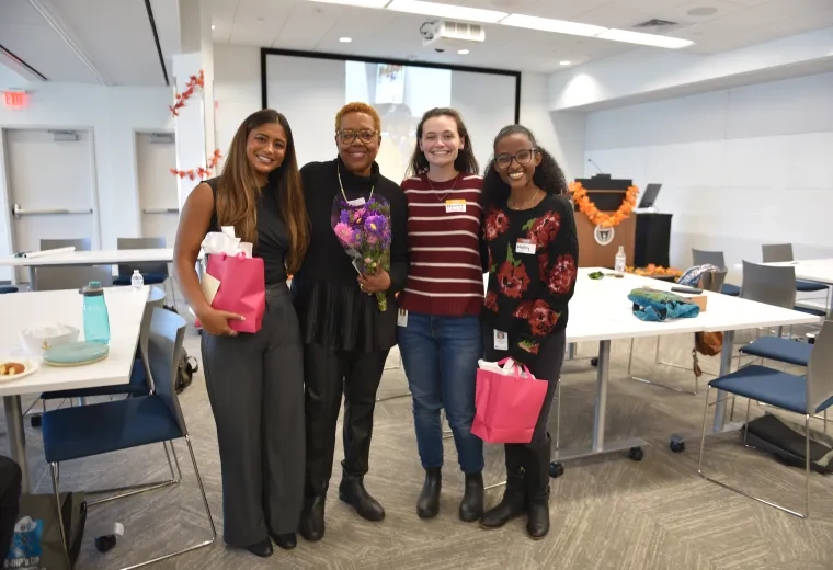Four people pose with tables behind them and two of them are holding pink gift bags