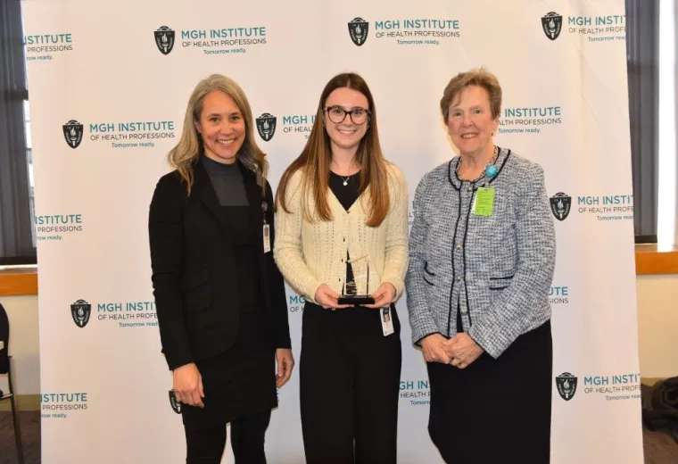 Three people stand in front of a background holding an award