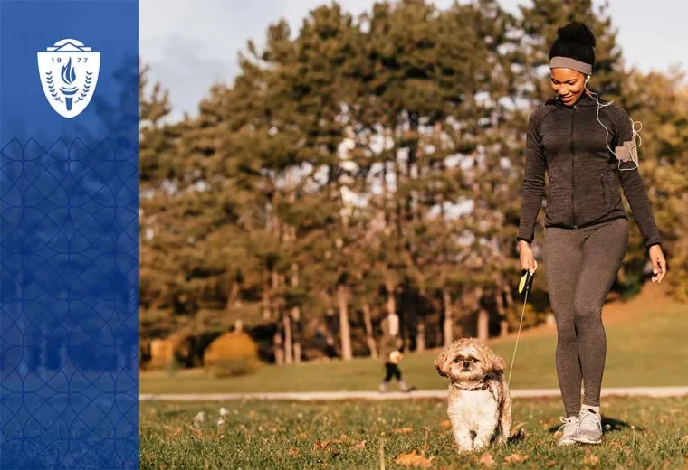 Woman wearing a black jacket and walking a dog on a leash in a park