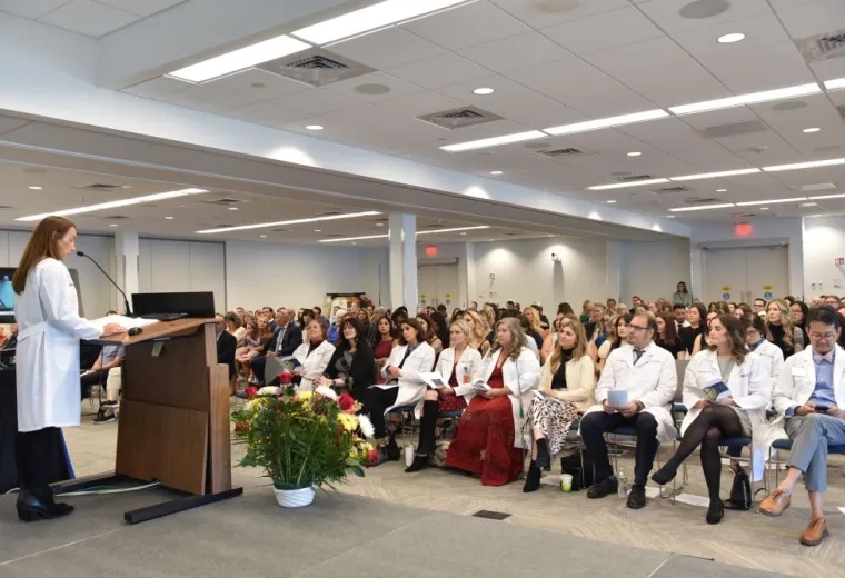 Woman standing at a podium addressing tens of people