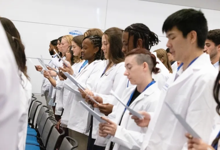 A line of people in white medical coats read from a piece of paper