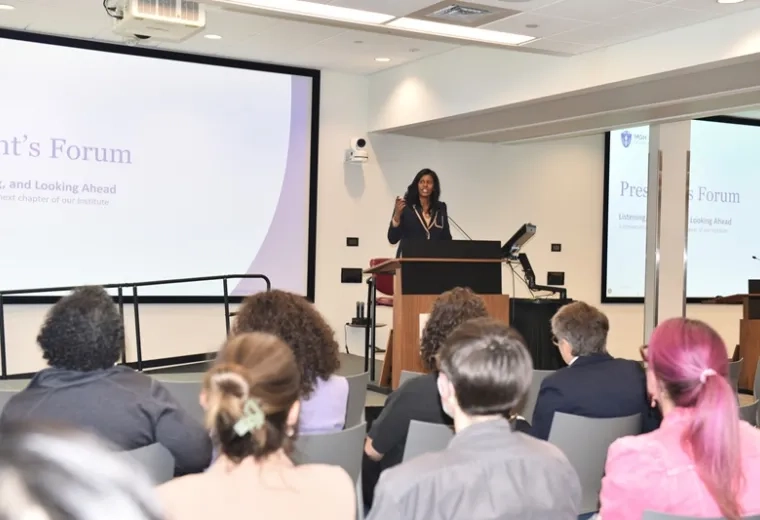 IHP President Deborah Jones speaking at a podium to seated forum attendees