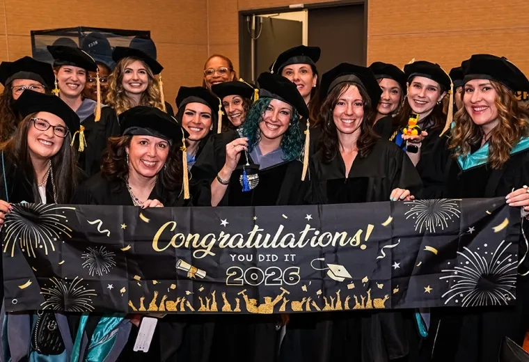 A group of people in graduation robes and hats hold a congratulations sign