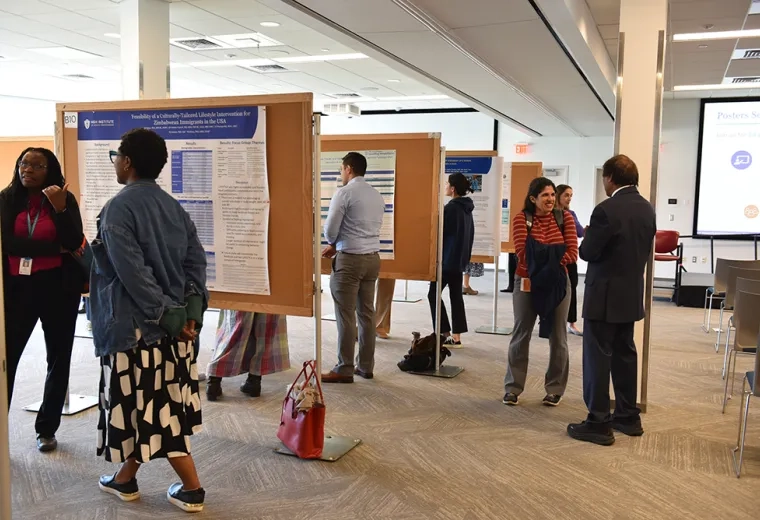 People stand at boards with scientific posters discussing their research with attendees