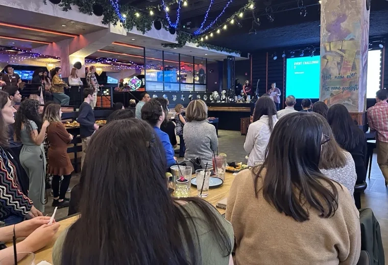 A crowd of people looks to the stage at the front of an employee event