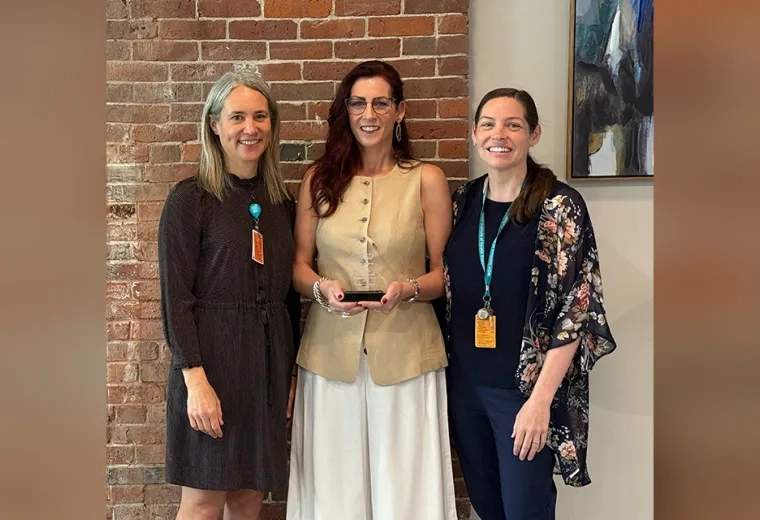 Three women pose with the one in the middle holding the Center of Excellence Faculty Excellence Award 
