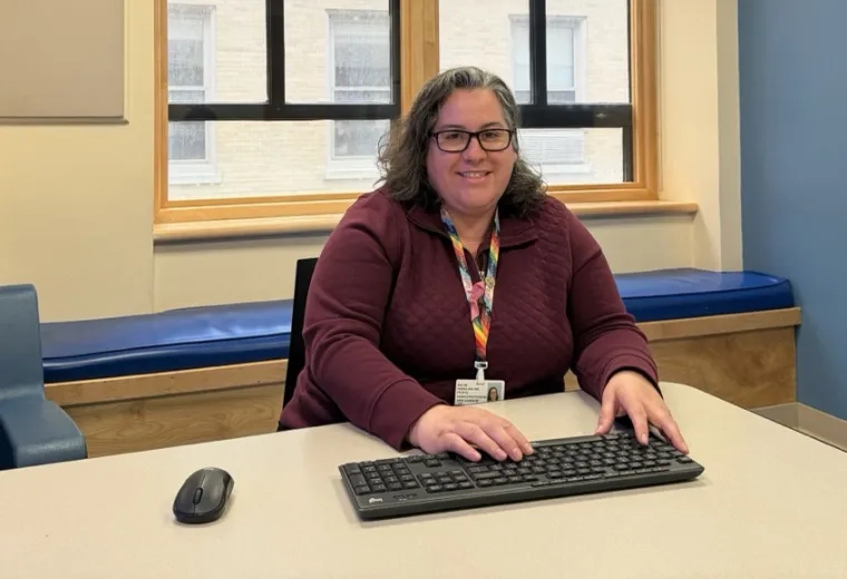 A woman sits at a table with a computer keyboard in front of her