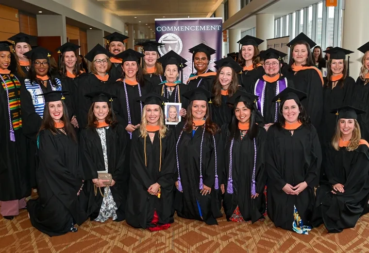 23 people wearing graduation gowns stand in three rows for a commencement photo