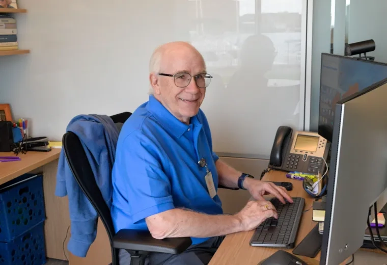 man in a blue shirt at a computer smiling 