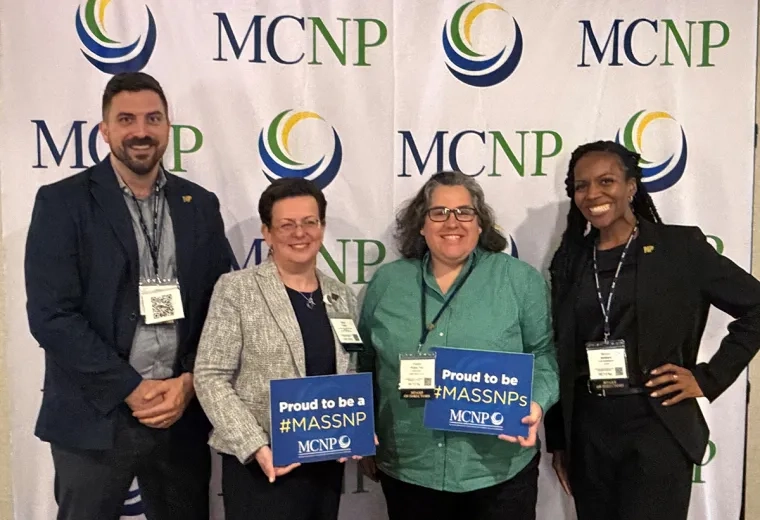 Four MGH Institute alumni pose for a photo in front of a banner for MCNP