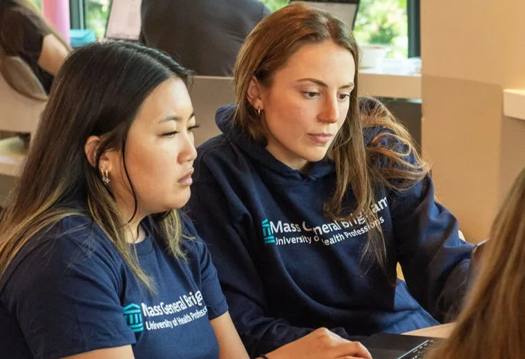 Two Mass General Brigham University students work during class wearing T-shirts with the university's name