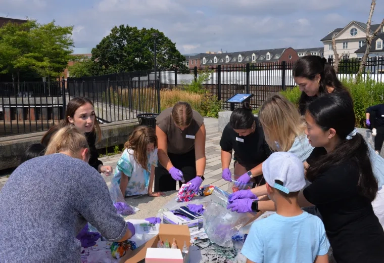 Kids and adults wear purple gloves and stand around a table dying shirts