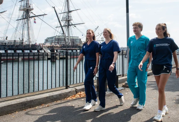 students in scrubs and tshirts walk in front of the constitution ship