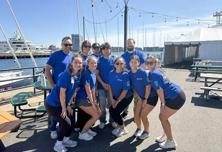 Volunteers in blue shirts posing in front of the Boston Harbor