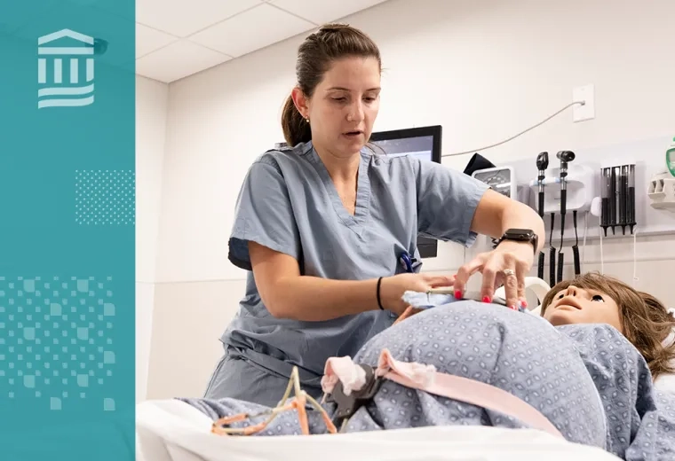 woman in scrubs adjusts a strap on a pregnant manikin in a hospital bed