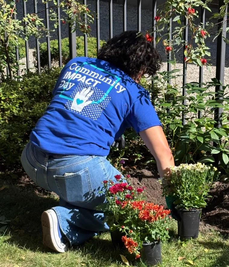 Woman in a blue t-shirt that reads "Community Impact Day" tending to a garden