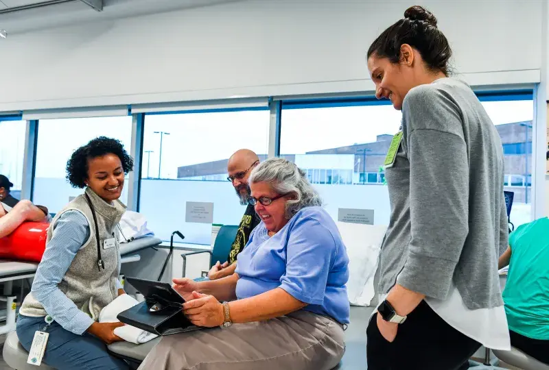 jane, seated, looks at a tablet while students stand around her