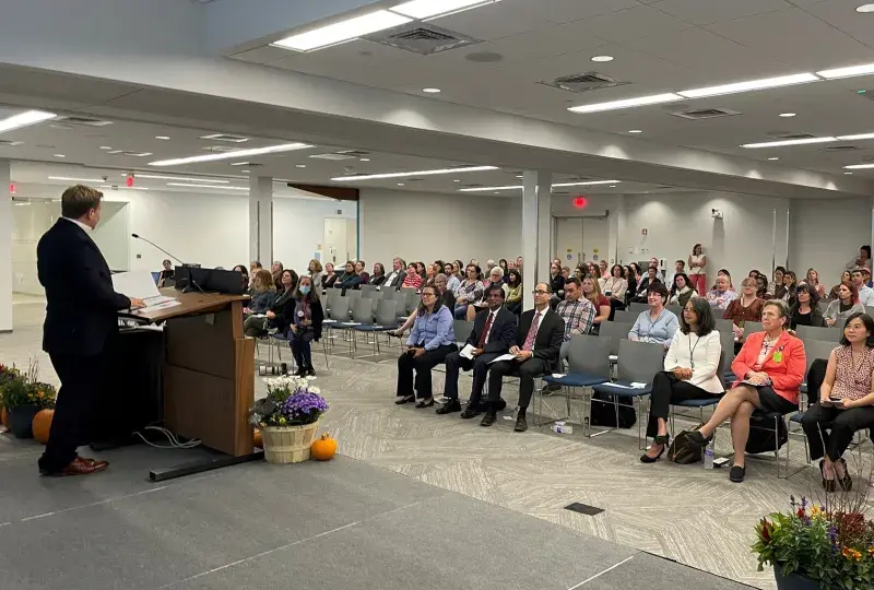 a large room with people seated listening to a man at a podium