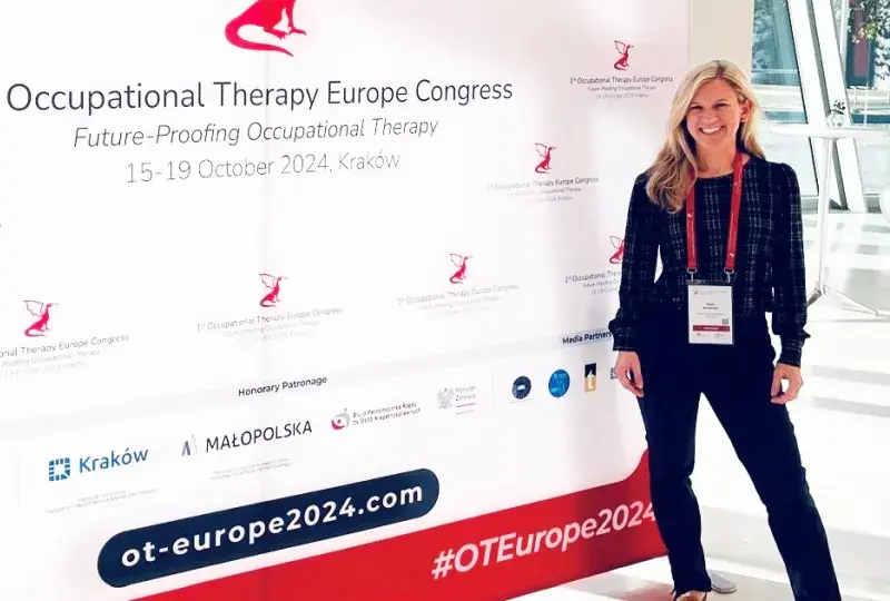 A woman stands in front of a sign for the 1st Occupational Therapy Europe Congress