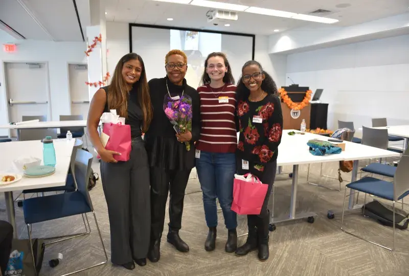 Four people pose with tables behind them and two of them are holding pink gift bags