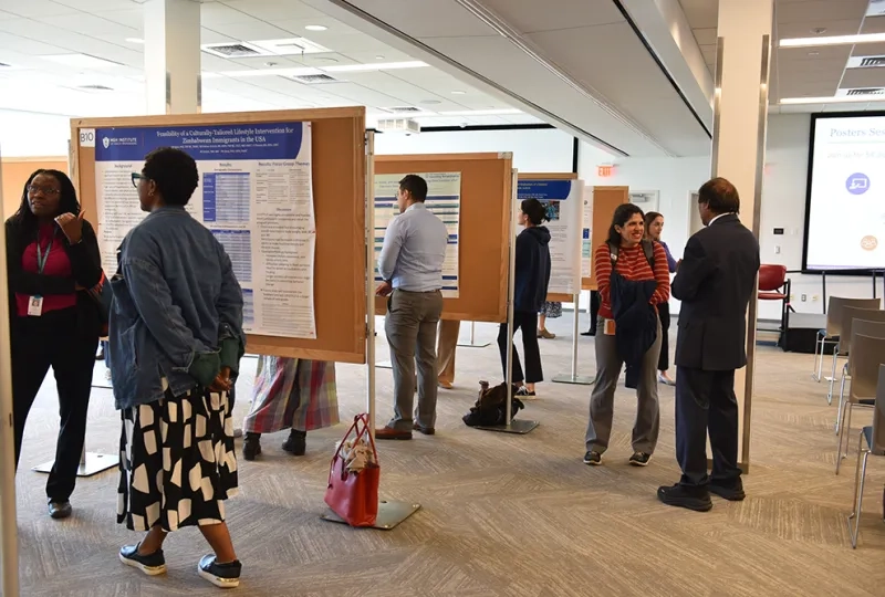 People stand at boards with scientific posters discussing their research with attendees
