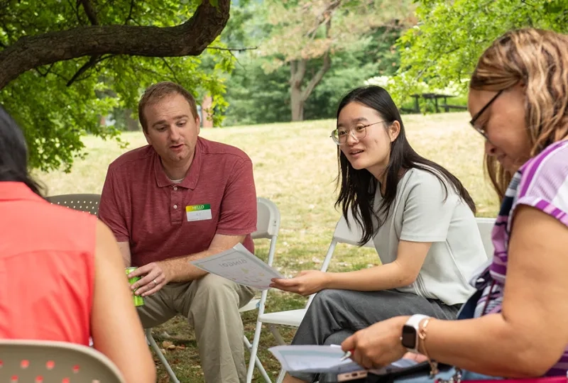 People sitting in chairs in a circle holding pieces of paper and talking to each other