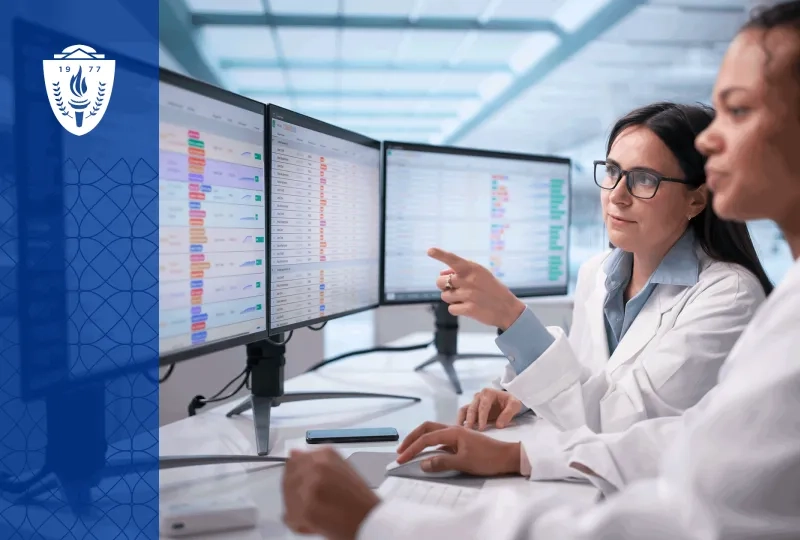 A healthcare educator stands with a small group of nursing and medical learners in a simulation lab reviewing learner analytics on a large display screen. The setting feels collaborative and academic, with realistic clinical equipment and human interaction rather than futuristic technology imagery. 