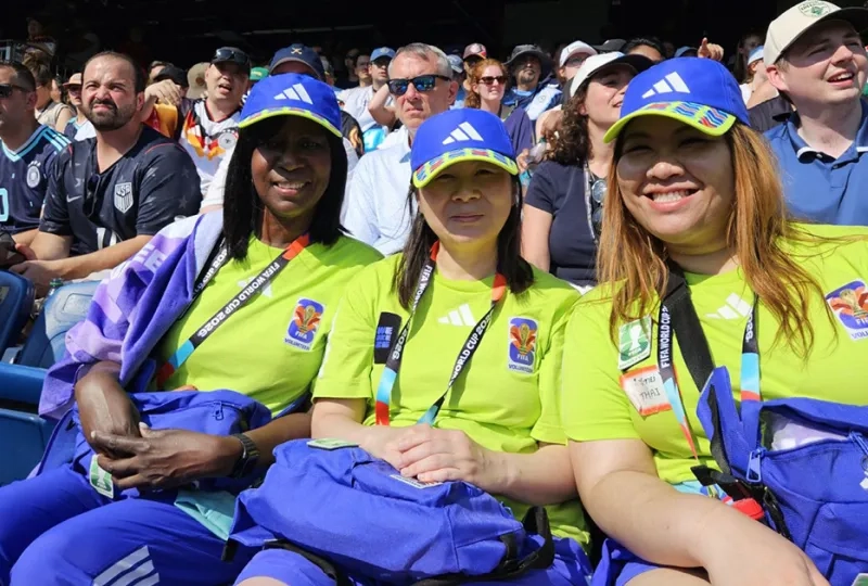 Three women sit in a stadium watching a World Cup game
