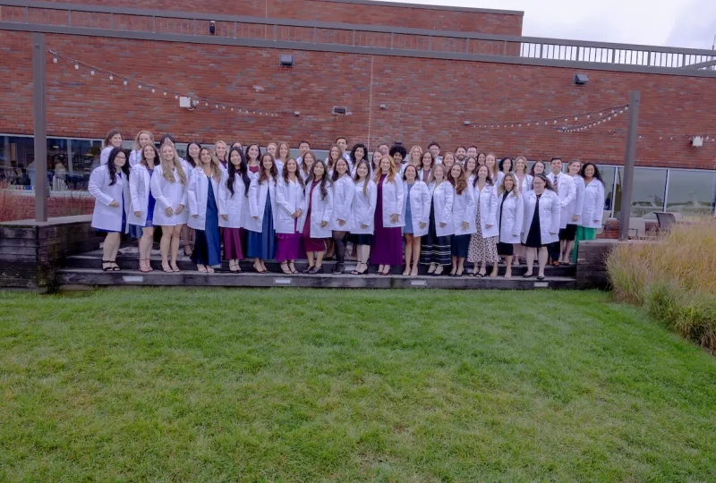 group photo of men and women in long white coats in front of a brick building with grass in front of them